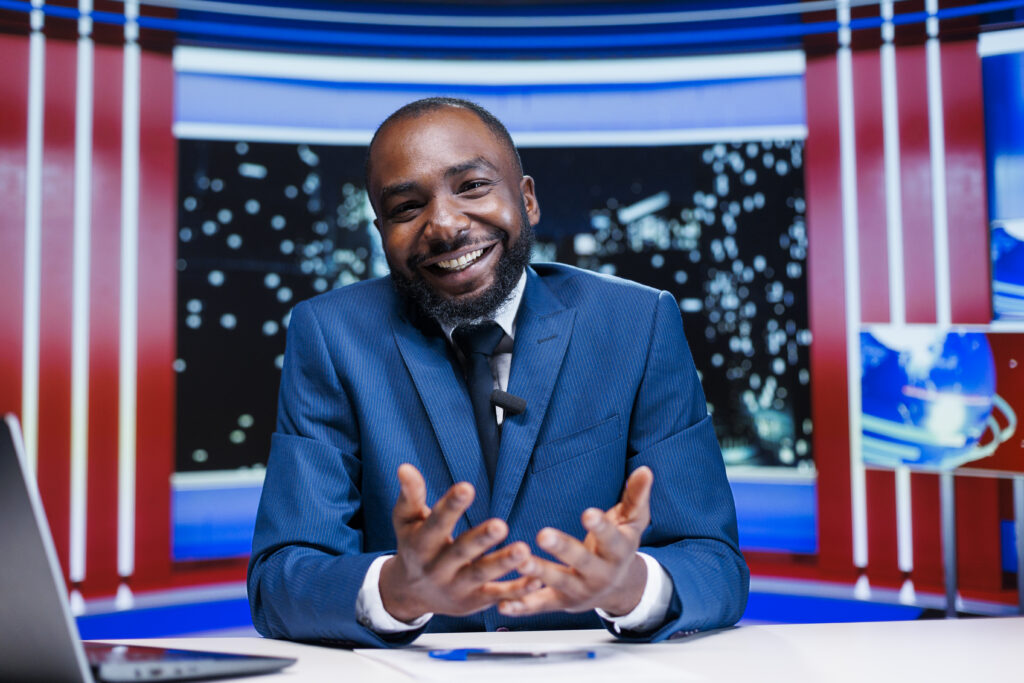 smiling-man-in-suit-gesturing-in-television-studio-2026-03-19-07-08-35-utc